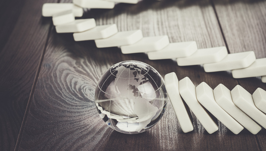 Small glass globe stopping a chain of falling white dominoes on a wooden surface.