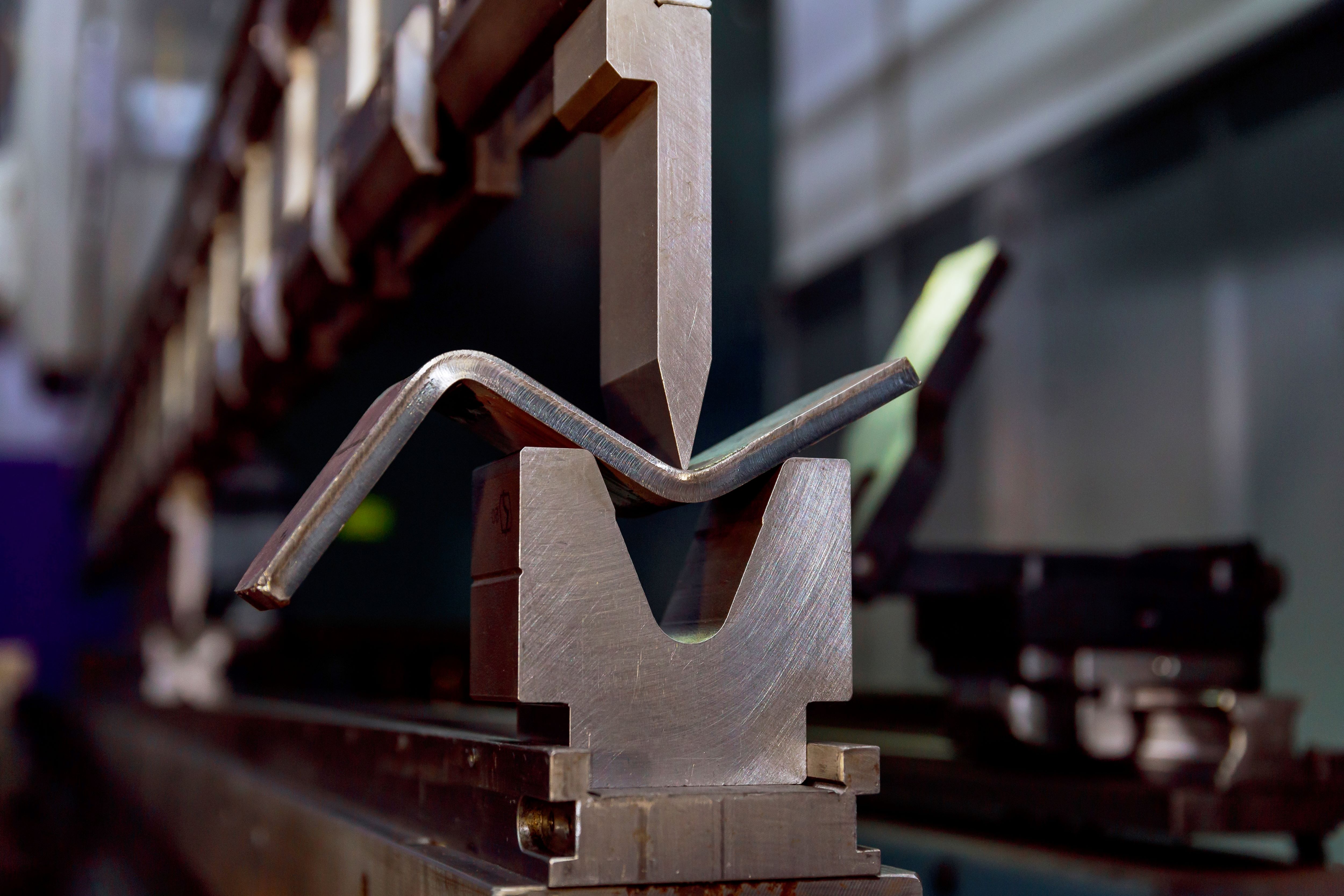 Industrial press brake forming a steel section by bending it between a shaped punch and die, highlighting the precision metalworking process used in fabrication and manufacturing.